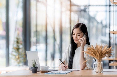 young asian business woman using laptop and writing on notebook, woman officer hard working communicate with customer and record