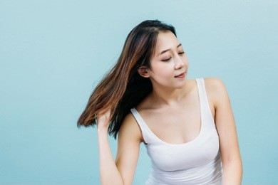 happy young woman touching her hair against blue pastel background