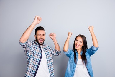 portrait of young caucasian, sweet, foolish, attractive, lovely, cute, crazy, successful partners celebrating victory with raised fists, screaming, shouting over grey background