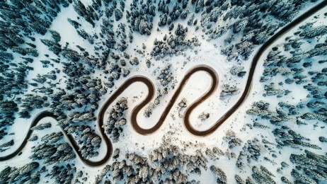 top aerial view of snow mountain landscape with trees and road. dolomites, italy.