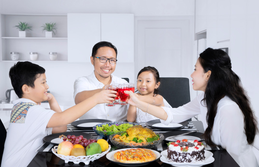 picture of asian family toasting glasses of syrup together before having meals while sitting in the kitchen