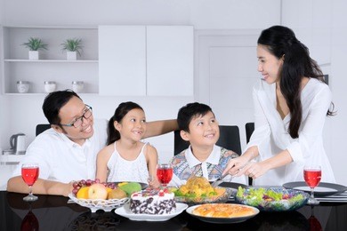 picture of young mother serving a roast chicken for her husband and children while having dinner together at home