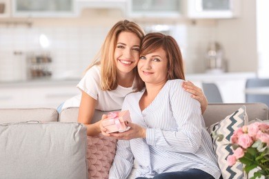 attractive young woman giving her mother gift box at home