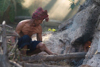 an old man burning firewood. a man's hand is laying wood inside the furnace and fireplace