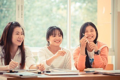 happy asian young woman doing group study. asian university or college students studying together with tablet,laptop and documents paper for report near windows in classroom. education class concept