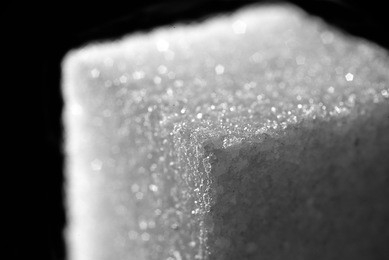 high resolution close up photo of sugar cube isolated on black background with flashlights. rim light flash made reflection with purity translucent of sugar crystals on sugar cube to show surface.