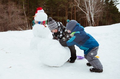 two young boys make a snowman on a winter day.
