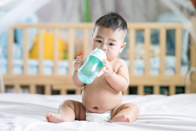 asian baby drink water by plastic bottle in bed room