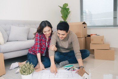 young asian couple sitting on the floor and looking at the blueprint of new home.