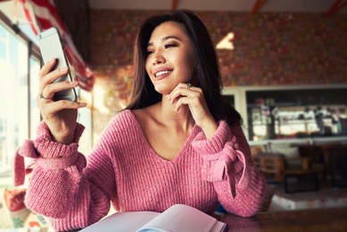 beautiful  asian woman using an application to send an sms message in her smartphone device while sitting in modern coffee shop.