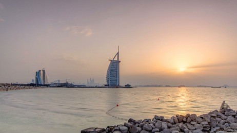 dubai skyline with burj al arab hotel during sunset timelapse. view from jumeirah beach. burj al arab is a luxury 5 stars hotel built on an artificial island in front of jumeirah beach.