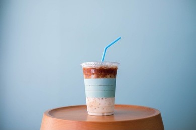 minimalism and pastel blue concept : a clear plastic cup of ice coffee latte with pastel blue straw on soft wooden chair with pastel blue background, close up, copy space