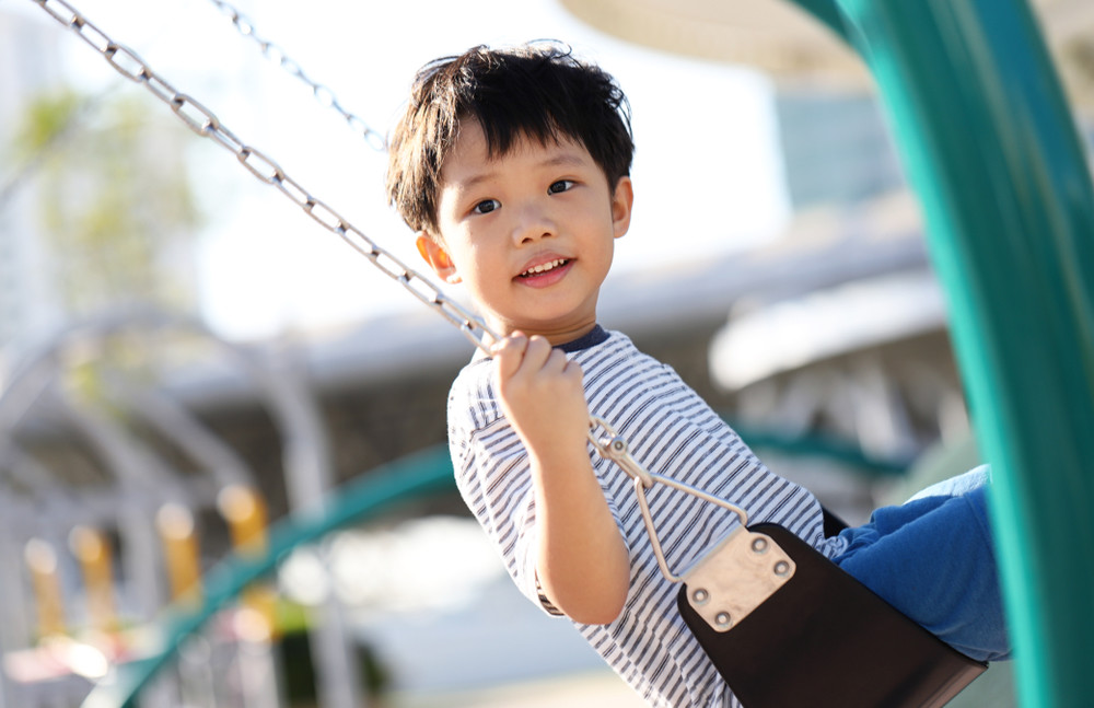 cute asian baby boy playing on a swing and having fun in a modern playground