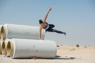 black african american athletic woman jumps over and leaps from construction pipes wearing sports outfit in a parkour or extreme fitness competition wearing a sports outfit.