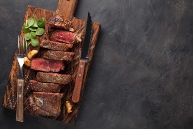 closeup ready to eat steak new york beef breeds of black angus with herbs, garlic and butter on a wooden board. the finished dish for dinner on a dark stone background. top view with copy space