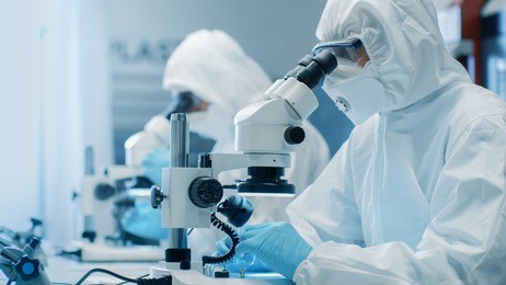 two engineers/ scientists/ technicians in sterile cleanroom suits use microscopes for component adjustment and research. they work in an electronic components manufacturing factory.
