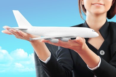 portrait of young happy woman stewardess holding jet aircraft in her arms on foreground. advertisement banner for transport companies