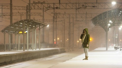young woman on empty railway platform in blizzard waiting for a train / girl missed a train / woman is waiting for the train in bad weather and talking on the phone 