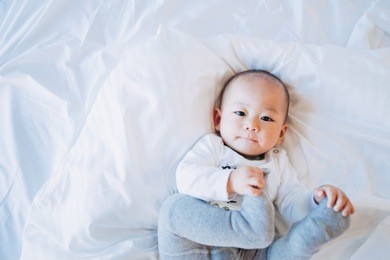 cute adorable nine months baby boy sucking finger and feet as getting first tooth.closeup of adorable boy child, little baby boy on the white bed.oral care concept.