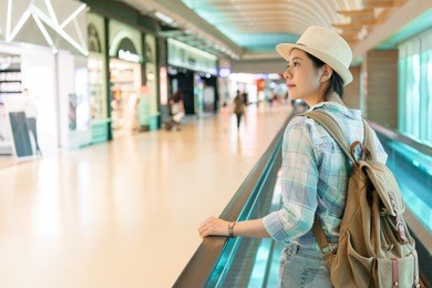 beautiful asian woman walking around airport. looking window shopping of the duty free shop on the escalator conveyor belt.