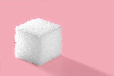 high resolution minimal looks close up photo of pure white sugar cube isolated on pink background with copy space. flash light made reflection with sugar crystals to show sugar cube surface.