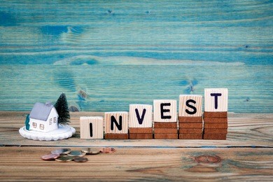 miniature model of house and wooden letter text: invest