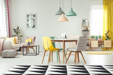 geometric carpet in cozy living room interior with pastel lamps above wooden table and yellow, mint and grey chair against a wall with poster