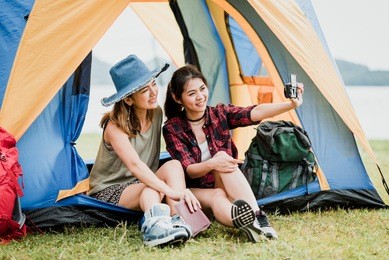 happy asian girl friends traveler smile for taking selfie during camping by the lake in tent.