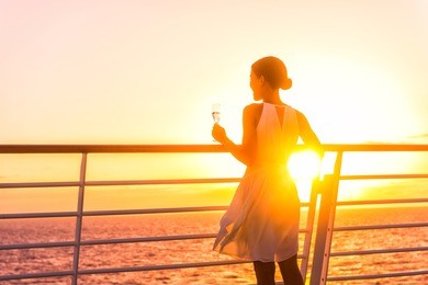 luxury cruise ship travel elegant woman drinking glass of champagne enjoying watching sunset from boat deck over ocean in europe destination vacation. cruising sailing away on holiday.