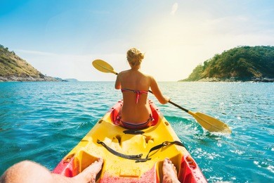 woman and man exploring calm tropical bay with limestone mountains by kayak. phuket, thailand.
