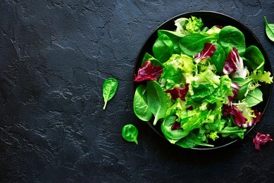 mix salad leaves in a black bowl over dark slate, stone or concrete background.top view with copy space.