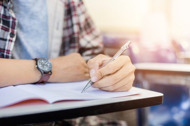 soft focus.high school or university student holding pencil writing on paper answer sheet.sitting on lecture chair taking final exam attending in examination room or classroom.student in casual