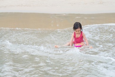 cute asian little girl is playing in the sea waves with fully happiness moment during vacation period, concept of happy and healthy kid and learning by traveling  for good experiences.