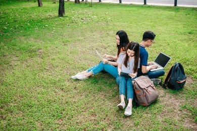 a group of young or teen asian student in university smiling and reading the book and look at the tablet or laptop computer in summer holiday.