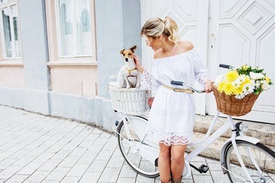 beautiful, blond woman riding a bicycle in a town with her dog 