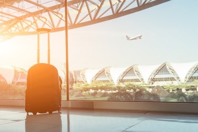 silhouette of luggage or suitcase placed at the window at waiting terminal in international airports in thailand with the airplan taking off behide the building.