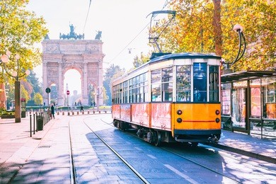 famous vintage tram in the centre of the old town of milan in the sunny day, lombardia, italy. arch of peace, or arco della pace on the background.