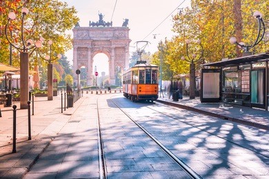 famous vintage tram in the centre of the old town of milan in the sunny day, lombardia, italy. arch of peace, or arco della pace on the background.