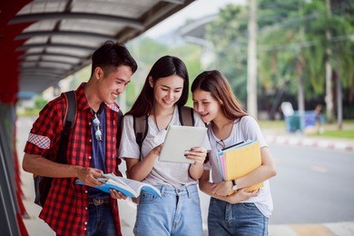 portrait of young asian student groupand are tutoring exam with study book and taplet, standing on the walk way in univercity. student group and tutoring education concept.