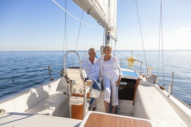 a happy senior couple laughing having fun sailing at the wheel of a yacht or sail boat on a calm blue sea
