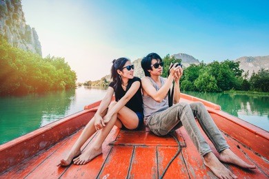 couple traveler sitting on the boat and taking photo view of river and mountain by camera on holiday.