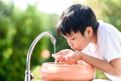 preteen asian boy take water from faucet to wash his mouth and drink in a garden.