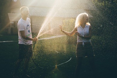 couple having fun. happy people with garden hose at sun set.