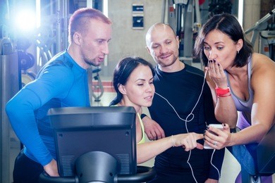 cheerful friends in the gym have fun and watch videos on the phone