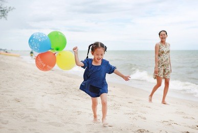 happy mother and daughter playing balloon on beach. holiday concept.