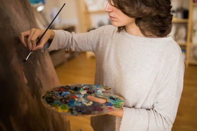 concentrated young caucasian woman painter working in canvas in art studio