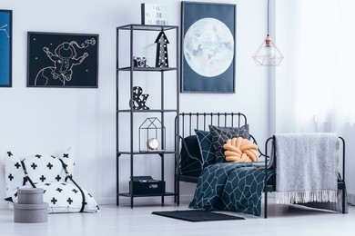 orange knot pillow on the bed next to shelves in astronaut's bedroom interior with poster of the moon