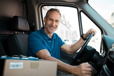 delivery man driving van with packages on the front seat. happy mature courier in truck. portrait of confident express courier driving his delivery van.