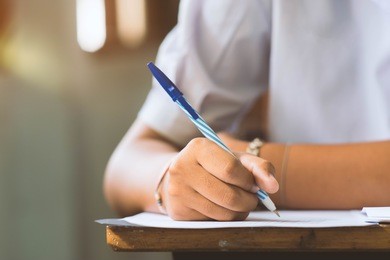 closeup to hand of student  holding pen and taking exam in classroom with stress for education test.