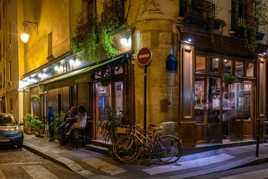 night view of cozy street with tables of cafe and old bicycle in paris, france
